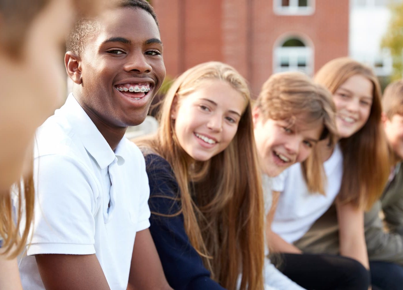 grouping of smiling teens sitting together outside